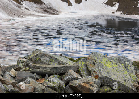 Voir l'encadré de l'oeil sur le lac de montagne de Rila, couverts par la glace fissurée, colorés, couverts de mousse et de l'arrière-plan au premier plan les rochers falaise couverte de neige Banque D'Images