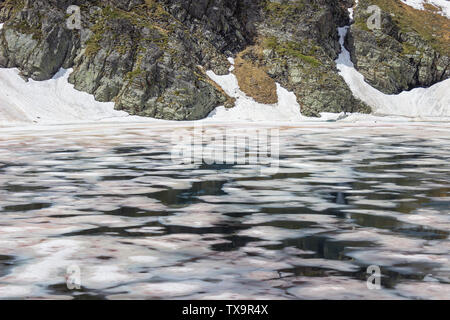 Vue en gros plan sur l'Œil lake, l'un des sept lacs de Rila, coloré, avec de la glace brisée à une falaise rocheuse couverte de neige Banque D'Images