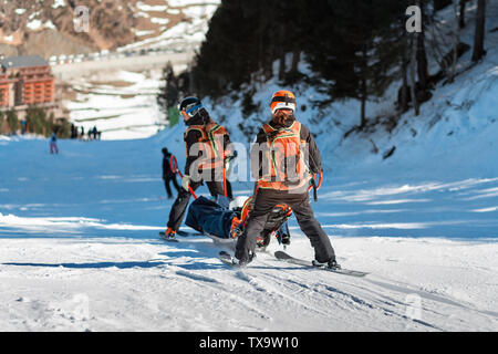 Les sauveteurs dans une station de ski d'évacuer la victime de la pente. Deux sauveteurs descendre un touriste sur une luge spécial sur une journée d'hiver ensoleillée. Blurred background Banque D'Images