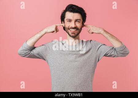 Beau jeune homme barbu agacé brunette wearing sweater isolés sur fond blanc, couvrir les oreilles Banque D'Images