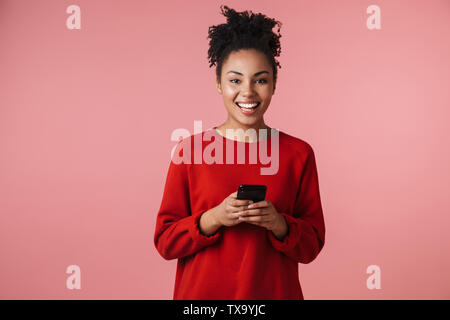 Image libre de charmant african american woman typing on cellphone smiling et plus isolé sur fond rose Banque D'Images