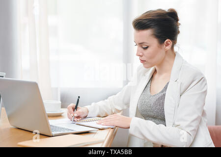 Concentrated businesswoman sérieuse en veste blanche sitting at table Banque D'Images