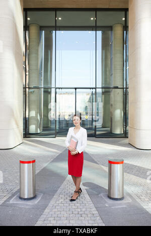 Portrait of young businesswoman standing in front of office building entrée privée, copy space Banque D'Images