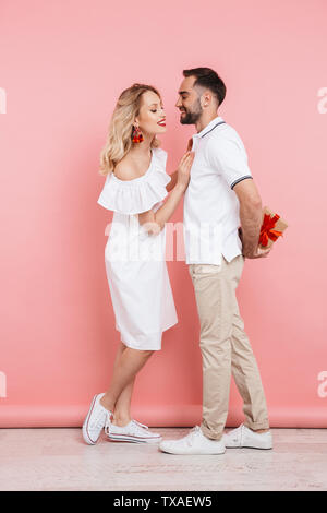 Toute la longueur d'un attrayant cheerful young couple isolé sur fond rose, donnant à l'heure actuelle, la célébration de Banque D'Images