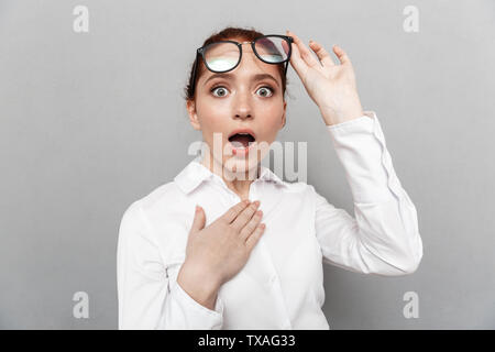 Image of redhead businesswoman wearing eyeglasses 20s demande à huis clos dans office isolated over grey background Banque D'Images