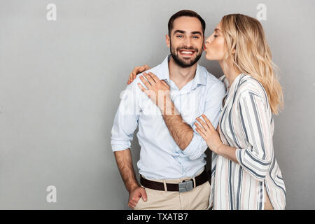 Image de joli couple dans des vêtements décontractés smiling while woman kissing bel homme isolé sur fond gris Banque D'Images