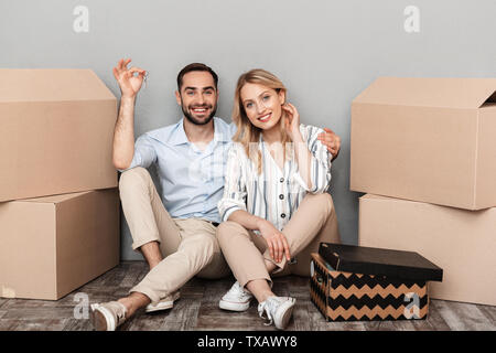 Photo de couple dans des vêtements décontractés coin près de boîtes de carton et la tenue touches plates plus isolé mur gris Banque D'Images