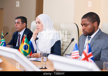 Pensive young female délégué en hijab qui écoute l'un de ses collègues Banque D'Images