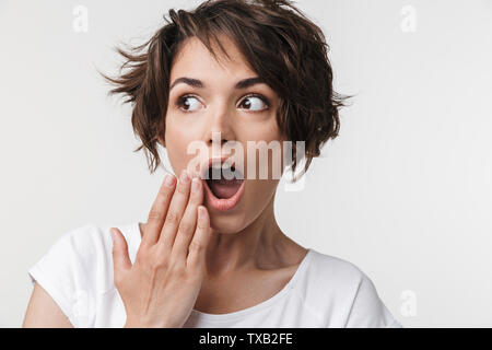 Portrait de femme avec surprise dans les cheveux bruns courts t-shirt de base couvrant sa bouche avec la main plus isolé sur fond blanc Banque D'Images