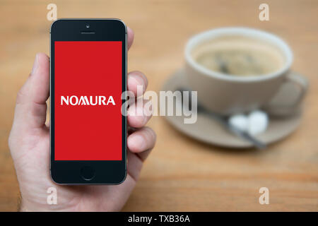 Un homme se penche sur son iPhone qui affiche le logo Nomura Holdings (usage éditorial uniquement). Banque D'Images