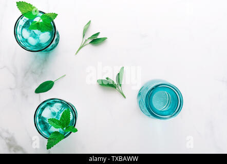 Vue de dessus deux belles turquoise vintage verres et une bouteille de boisson froide et des cubes de glace, décoré de feuilles de menthe verte fraîche sur du marbre blanc Banque D'Images