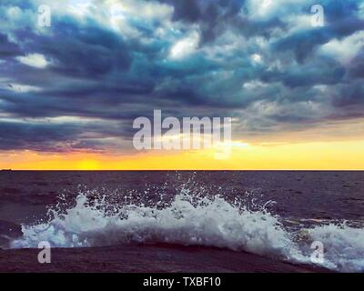 Un paysage très rare, le soleil est couvert par d'épais nuages sombres, avec seulement un peu d'incandescence, le clapotis des vagues sur les rochers, les vagues éclaboussant autour Banque D'Images