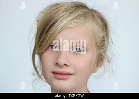 Portrait d'une jeune fille blonde aux yeux bleu maladroitement regardant la caméra sur un fond blanc. Banque D'Images