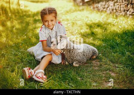 Beau et mignon fille en robe bleue avec de belles coiffures et make-up assis dans un beau jardin verdoyant et jouant avec une chèvre Banque D'Images