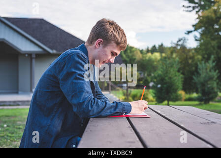 Adolescent heureux de faire le travail scolaire en plein air sur un après-midi ensoleillé. Banque D'Images