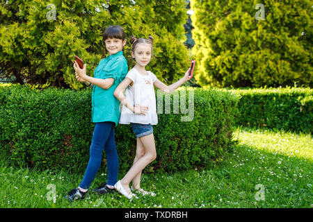 Deux jolies filles d'âge scolaire se photographier sur le téléphone près de la Verdure Banque D'Images