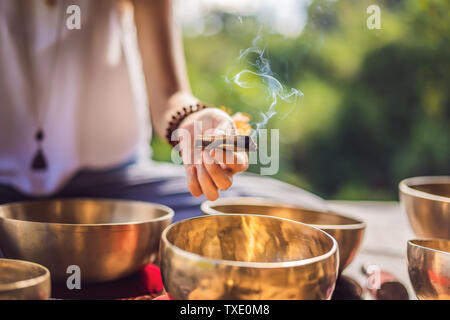 Femme jouant sur bol chantant tibétain, assis sur un tapis de yoga contre une chute d'eau. Vintage tonned. Belle fille avec perles mala méditer Banque D'Images