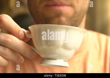 L'homme boit la tasse de thé et tient dans ses mains dans la douce lumière du soleil dans le café Banque D'Images