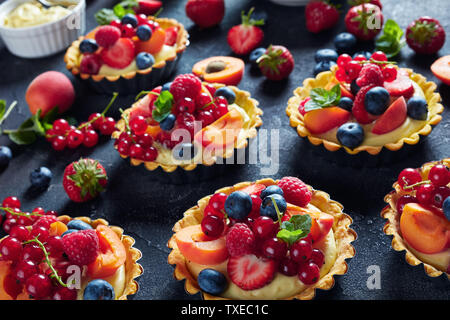 Close-up de l'été anglais desserts - tartelettes au citron crème anglaise à la crème garnie de framboises, abricots, de bleuet, de fraise, de groseille rouge Banque D'Images