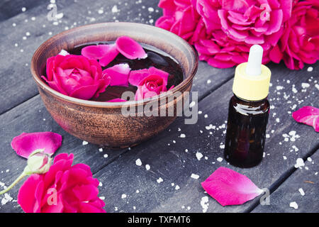 Près de l'huile essentielle de pétales de rose rouge bol avec sur un fond en bois sombre. L'aromathérapie. Banque D'Images