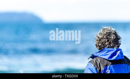 Vue arrière d'une femme mature aux cheveux gris regardant la mer avec un bleu estompé dans l'arrière-plan, magnifique journée ensoleillée en Irlande Banque D'Images