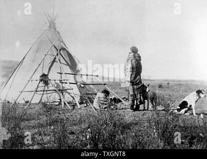 Le cri des Indiens de l'Amérique du Nord avec sa squaw papoose sur son dos, debout devant son tipi avec un enfant plus âgé et deux chiens. A partir de photo prises c1885-1890 Banque D'Images