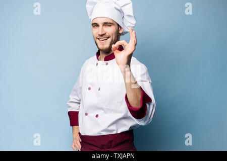 Professionnel positif homme heureux savoureux chef showing ok sign isolé sur bleu clair. Banque D'Images