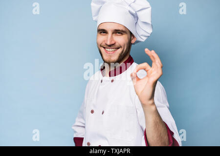Professionnel positif homme heureux savoureux chef showing ok sign isolé sur bleu clair. Banque D'Images