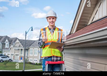 Young male architect standing sur une échelle et vêtus de vêtements de sécurité. Banque D'Images
