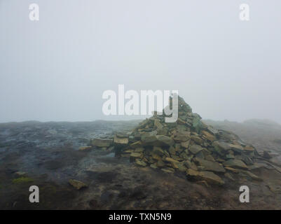 Tas de pierres sur le sol boueux entouré de brume sur le haut de pic Hoverla dans les Carpates, l'Ukraine. Banque D'Images