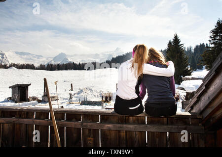 Deux skieurs adolescente assis sur une terrasse sur le toit de cabine en paysage couvert de neige, vue arrière, Tyrol, Styrie, Autriche Banque D'Images