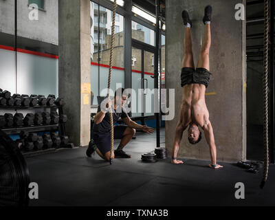 La motivation de l'homme ami doing handstand in gym Banque D'Images