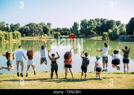 Groupe d'amis de sauter devant un lac en park Banque D'Images