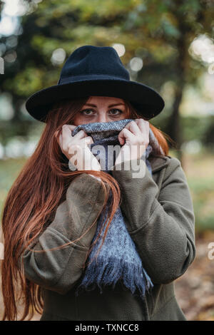 Jeune femme aux longs cheveux rouges en automne parc couvrant la bouche avec de l'écharpe, portrait Banque D'Images