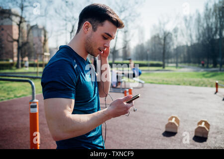La gymnastique au sport en plein air, jeune homme à l'écoute de l'écouteur et looking at smartphone Banque D'Images