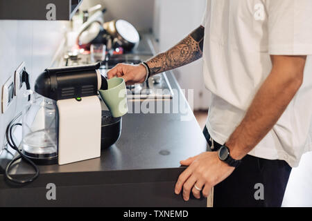 Mid adult man pouring coffee à partir de la machine à café sur le comptoir de la cuisine, mid section Banque D'Images