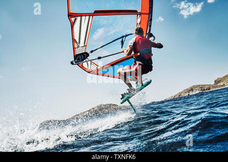 Jeune homme mid air planche à voile, les vagues de l'océan, vue latérale, Limnos, Calino, Grèce Banque D'Images