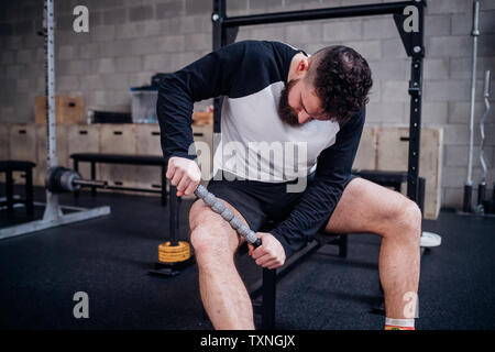 Jeune homme de cuisse avec rouleau de massage musculaire stick in gym Banque D'Images