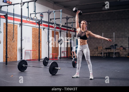 Jeune femme d'haltères avec un bras de levage in gym Banque D'Images
