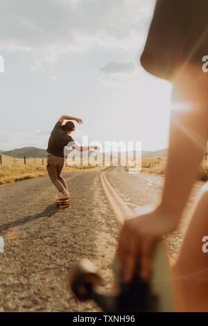 Les jeunes hommes nus skate skateboarder on rural road, petite amie observant, Exeter, California, USA Banque D'Images