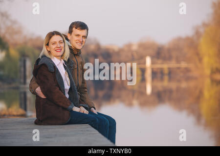 Cute couple sitting at Riverside sur coucher de soleil en automne chaud soir date romantique. Banque D'Images