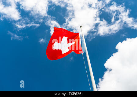 Dans le vent à gauche, le drapeau de la Suisse accrochée au mât, sur le fond bleu du ciel avec des nuages blancs. Banque D'Images