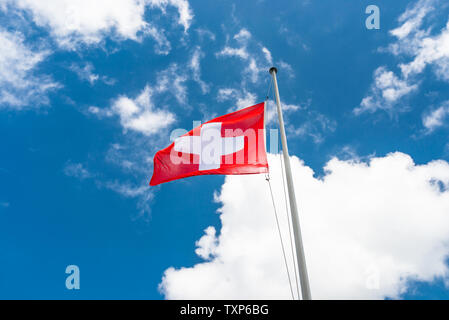 Dans le vent à gauche, le drapeau de la Suisse accrochée au mât, sur le fond bleu du ciel avec des nuages blancs. Banque D'Images