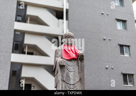 Osaka, Japon statue Jizo avec dossard rouge isolé sur fond d'immeuble moderne au centre-ville de ville Banque D'Images