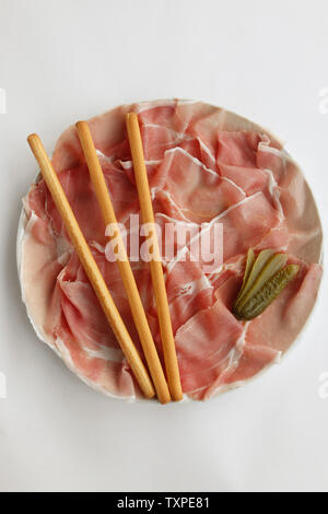 Plateau de Prosciutto di Parma (frais, jambon de Parme) avec des bâtonnets de pain en tranches et un cornichon isolé sur fond blanc. Banque D'Images