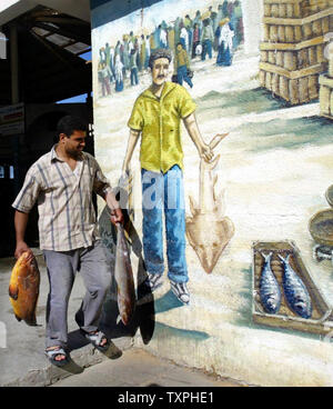 Un pêcheur palestinien détient un gros poisson que les acheteurs font des offres pour les lots de poissons qui sont mis en face d'un marché de poissons local près de la ville de Gaza, 17 Septembre, 2004 port. Des centaines d'acheteurs potentiels convergent sur le marché aux poissons à soumissionner sur des plateaux de poissons qui ont été capturés pendant la nuit au large de la côte de la bande de Gaza. Quelque 4 000 pêcheurs vivent au large de la mer dans la bande de Gaza dans une petite zone de pêche qui a été désigné par les autorités israéliennes. (UPI Photo/ Ismael Mohamad). Banque D'Images