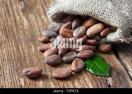 Les fèves de cacao (chocolat) dans un sac sac sur une table en bois. Banque D'Images