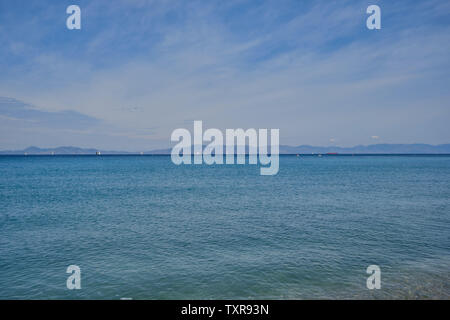 Mer calme de couleur turquoise et quelques nuages dans le ciel bleu, les voiliers et les montagnes au loin en arrière-plan Banque D'Images