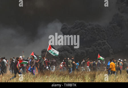 Des manifestants palestiniens brûlent des pneus pour se protéger des tirs de soldats israéliens que d'autres drapeaux nationaux de procéder à la frontière Israel-Gaza à Khan Younis, dans le sud de Gaza, le 6 avril 2018. Les troupes israéliennes ont tué trois Palestiniens et en a blessé des dizaines d'autres que des affrontements ont éclaté sur la frontière Gaza-Israel encore, selon des sources médicales. Photo par Ismael Mohamad/UPI Banque D'Images