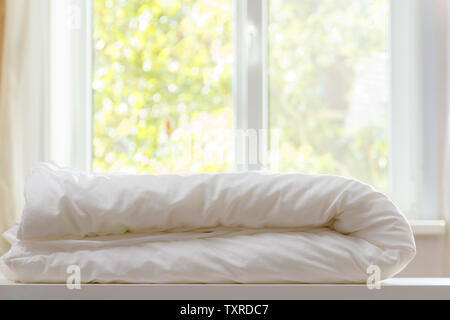 Un duvet blanc est posé sur la commode contre l'arrière-plan flou de la fenêtre. Banque D'Images